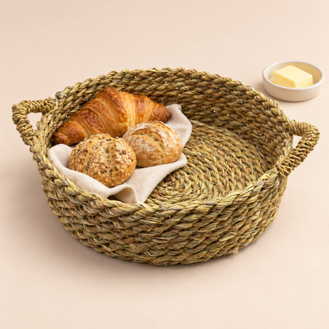 Woven Storage Basket with Handles styled with bread and linen on a warm beige studio background.